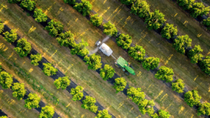 Zeleno rumeni traktor John Deere 5015EN, prikazan iz zraka, ki vleče pršilnik skozi enakomerno razporejene vrste v sadovnjaku