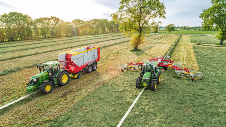 Traktorja John Deere z rotacijskim zgrabljalnikom in krmnim vozičkom na polju, pogled od zgoraj.
