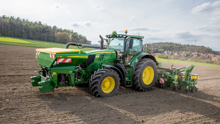 Traktor John Deere pri delu z zadaj nameščenim trosilnikom med obdelavo pripravljenega polja