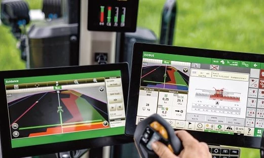 Dva zaslona na dotik v kabini John Deere, ki prikazujeta vodenje stroja in upravljanje priključka ter upravljavec pri delu z večfunkcijsko ročico