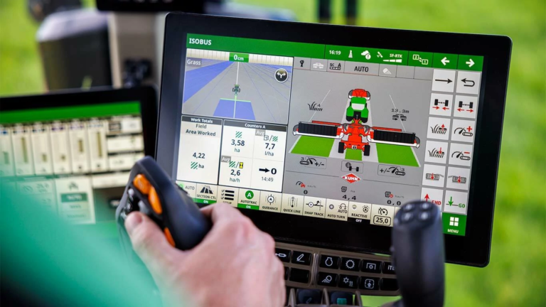 Zaslon na dotik John Deere v kabini s prikazom krmiljenja stroja in vmesnika za vodenje ter upravljavec pri delu z večfunkcijsko ročico