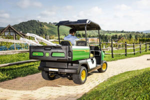 Pogled z zadnje strani na vozilo John Deere Gator GS, ki vozi po tlakovani poti s slikovitimi griči in vinogradi v ozadju.