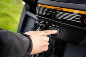 Prst, ki pritiska gumb za izbiro vožnje naprej na upravljalni plošči vozila John Deere Gator GS z električnim motorjem.